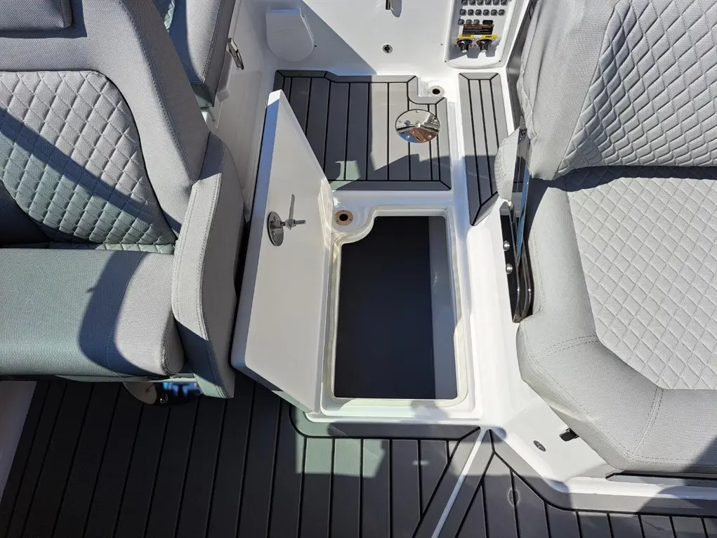 Interior of a boat featuring grey seating, an open storage compartment, and a textured deck surface.